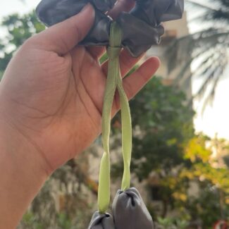 Hand holding a gray fabric flower garland with green fabric stems outdoors.1