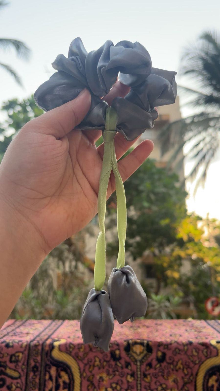 Hand holding a gray fabric flower garland with green fabric stems outdoors.1