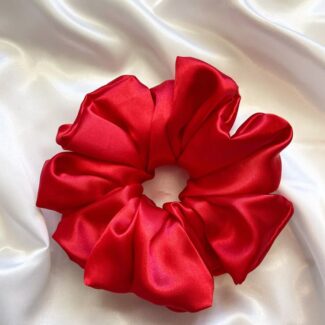 Red satin scrunchie laid on white silky fabric, circular and voluminous with gathered folds.