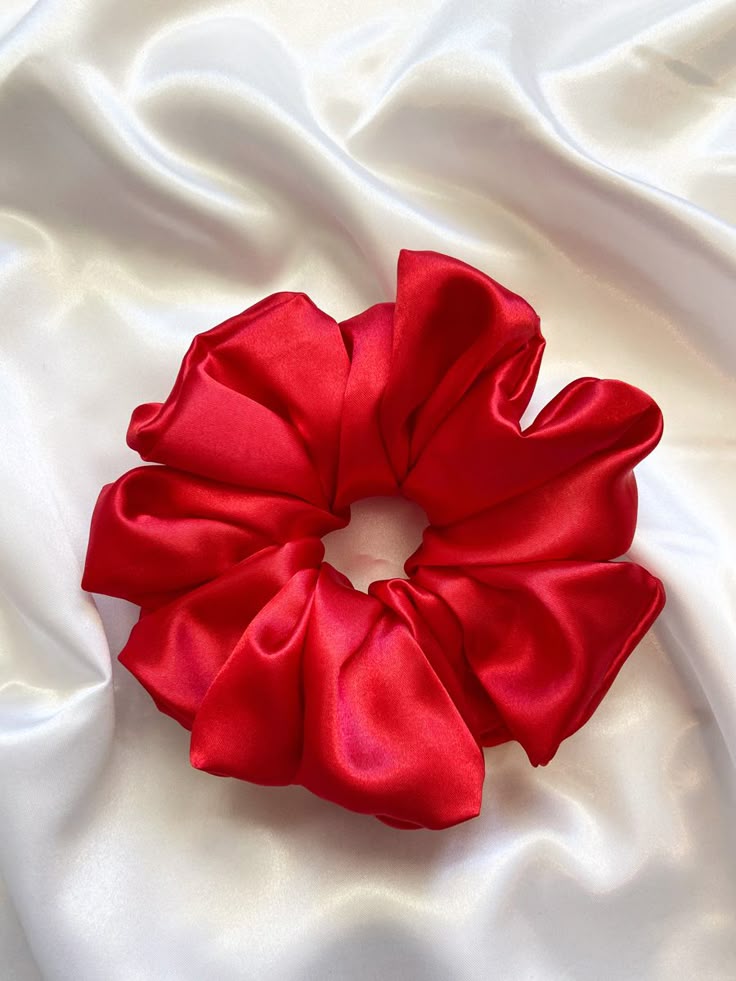 Red satin scrunchie laid on white silky fabric, circular and voluminous with gathered folds.