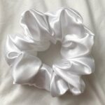 White satin hair scrunchie arranged in a circular shape on a light background